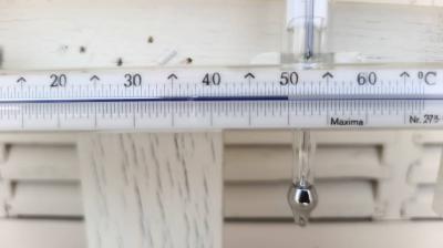 A close-up of a thermometer showing a temperature reading of approximately 49 degrees Celsius against a white wooden background.