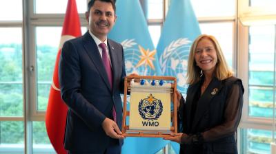 Two people stand indoors holding a framed WMO emblem, with the Turkish and WMO flags visible in the background.