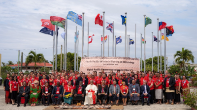 A large group of people pose for a photo in front of international flags and a banner for the Pacific Ministerial Meeting on Meteorology.