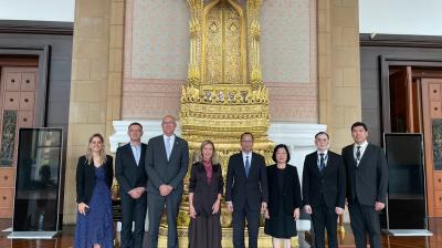 Eight people in formal business attire pose in a line in front of an ornate, gold-leafed ceremonial throne.