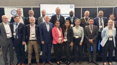 A group of eighteen conference attendees stand in two rows for a portrait in front of a presentation screen.