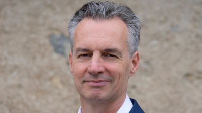 Headshot of a middle-aged man with short grey hair, wearing a white shirt and a blue blazer.