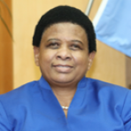 A woman in a blue suit sitting in front of a flag.