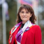 A woman in a red jacket standing in front of flags.