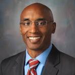 A black man in a suit and tie smiling.