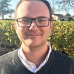 A man in glasses standing in front of a vineyard.