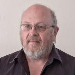 A man with glasses and a beard is standing in front of a white wall.