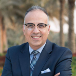 A man in a suit and tie poses in front of palm trees.