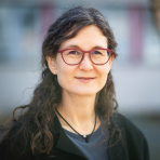 A woman in glasses is smiling in front of a tree.