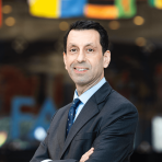 Kaveh Zahedi in a suit standing in front of flags.