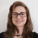 Luciana Gatti wearing glasses and pearls smiles for the camera.