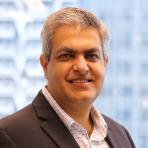 Amit Prothi in a business suit smiling in front of a window.