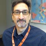 A man with glasses and an orange lanyard in front of a map.