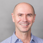 A bald man smiling in a blue shirt.