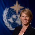 A woman smiling in front of a blue flag.