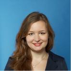 A professional portrait of a smiling woman with shoulder-length hair against a blue background.
