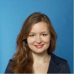 A professional portrait of a smiling woman with shoulder-length hair against a blue background.