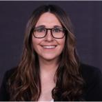 A smiling woman with long, wavy hair and glasses against a gray background.