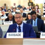 A delegate from barbados seated at a conference with a microphone and nameplate in front of him.