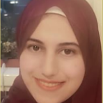 A person wearing a maroon headscarf and smiling at the camera, with a blurred background of indoor and outdoor elements.
