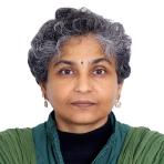 A person with short, curly gray hair and a green jacket looks directly at the camera against a plain white background.