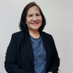 A woman with shoulder-length dark hair, wearing a black blazer over a blue lace top, poses against a plain white background, smiling at the camera.