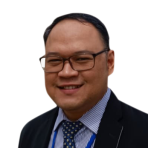 A man wearing glasses, a suit, a striped shirt, and a polka-dot tie, smiling at the camera against a white background.
