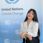 A woman kneels in front of a United Nations Climate Change backdrop, posing for a photo indoors.