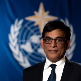 Alok Kumar Ojha standing in front of WMO flag.