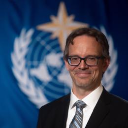 Daniel Kull standing in front of WMO flag.