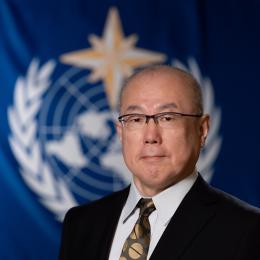 Tatsuya Kimura standing in front of WMO flag.