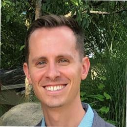 A man smiling in front of a tree.