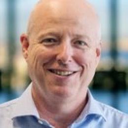 A bald man in a blue shirt is smiling.