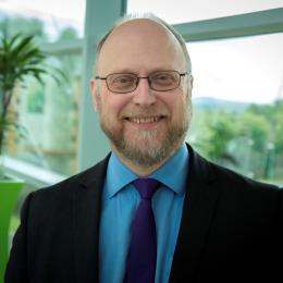 A bald man with glasses and a purple tie.