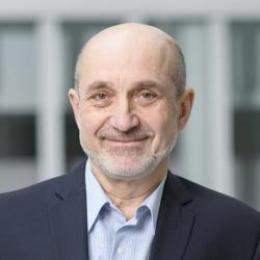 A bald man in a suit standing in front of a building.