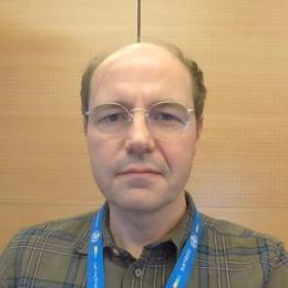 A man wearing glasses and a blue lanyard.