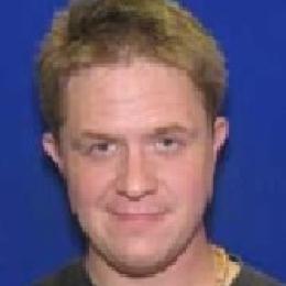A man in a black shirt is standing in front of a blue background.