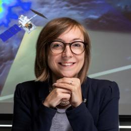 A woman in glasses is standing in front of a projection screen.