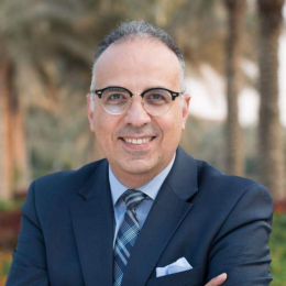A man in a suit and tie poses in front of palm trees.