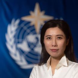 A woman in a white shirt standing in front of a flag.
