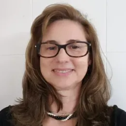 Luciana Gatti wearing glasses and pearls smiles for the camera.