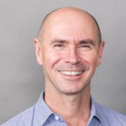 A bald man smiling in a blue shirt.