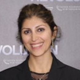A woman in a black suit standing in front of a wall.
