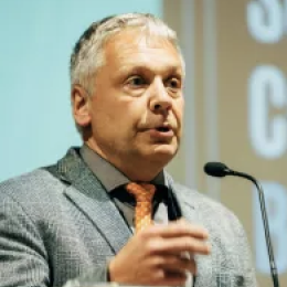 A man in a suit and tie speaking into a microphone.