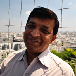 An indian man smiling in front of a fence.