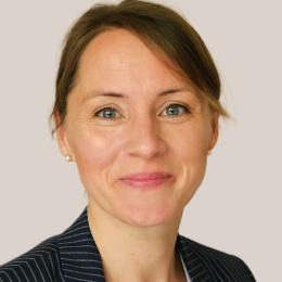 Headshot of a woman with short brown hair, wearing a pinstriped blazer and a white top, smiling at the camera against a plain background.