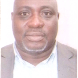 A man with a shaved head, short beard, and wearing a suit jacket over a light-colored shirt, facing the camera against a plain white background.