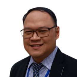 A man wearing glasses, a suit, a striped shirt, and a polka-dot tie, smiling at the camera against a white background.