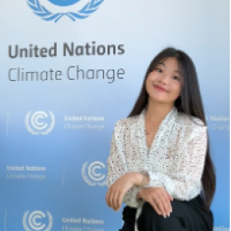 A woman kneels in front of a United Nations Climate Change backdrop, posing for a photo indoors.