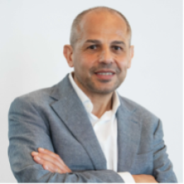 Man in a gray suit jacket and white shirt standing with arms crossed, smiling at the camera against a plain light background.